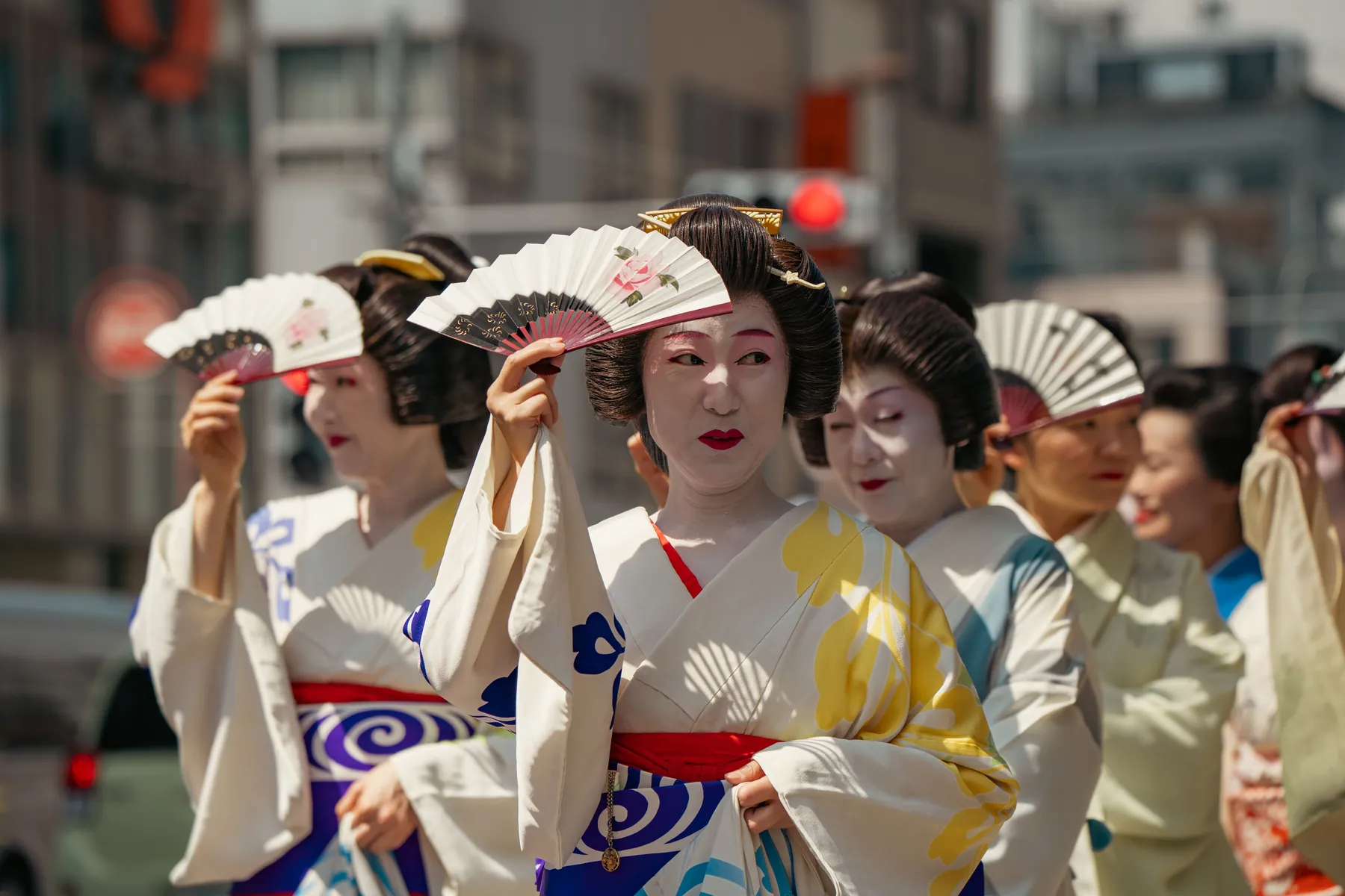 Kvinder i kimono og traditionelle frisurer skygger for ansigtet med foldevifter under en gadeparade i Tokyo