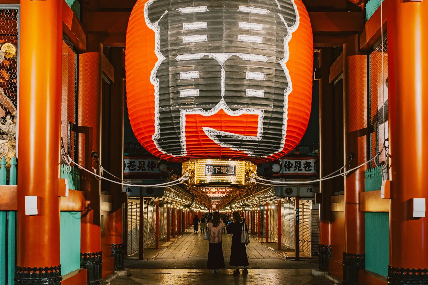 En kæmpe rød papirlanterne hænger over en oplyst gangsti kantet med butikker i Asakusa, Tokyo
